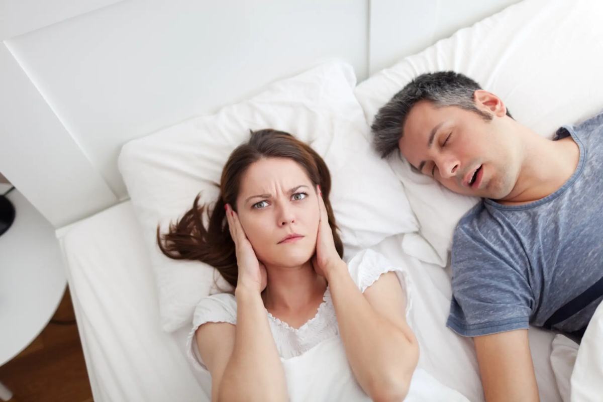 A woman covering her ears while her partner snores
